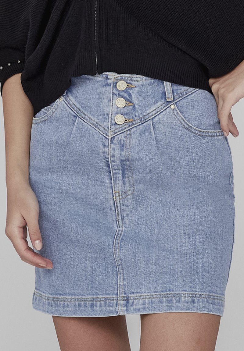 Gros plan d'une personne portant une jupe en jean bleu clair taille haute avec trois boutons sur le devant et un haut noir.