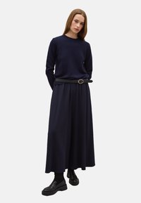 Navyblauwe trui met een ronde hals, gecombineerd met een vloerlange navy rok met een ceintuur in de taille en zwarte chunky schoenen.