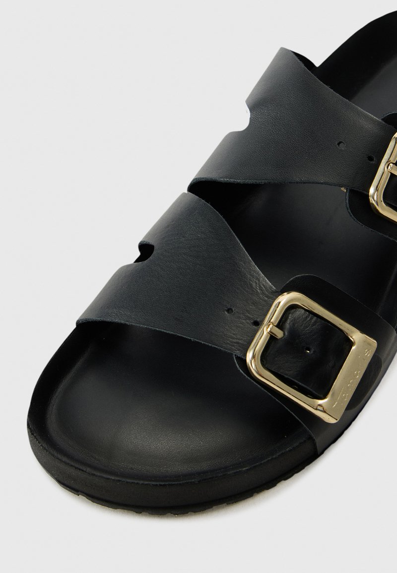 Schwarze Ledersandale mit zwei breiten Riemen und Ausschnittdesigns sowie goldfarbenen Schnallen. Glatte Oberfläche mit rutschfester Sohle.