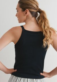 Débardeur côtelé marine avec des bretelles fines et une coupe ajustée. Le tissu a une texture lisse. La vue arrière montre les détails de l'encolure et des épaules.