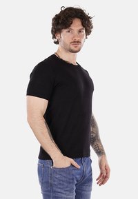 Camiseta de tirantes corta negra en tejido texturizado, con cuello redondo y corte relajado, combinada con jeans de color azul claro.