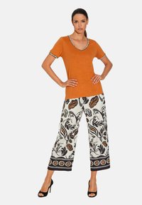 Oranje v-hals t-shirt met contrasterende zwart-witte rand, gecombineerd met wijde broek met een bloemenpatroon in zwart en bruin op een witte achtergrond.