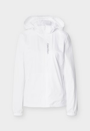 Hvit hettejakke med glidelås, elastiske mansjetter og sidelommer med glidelås, med "Calvin Klein"-logo trykt vertikalt ved siden av glidelåsen.