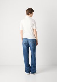 Hvit polo skjorte med korte ermer, kombinert med løse blå denimjeans. Jeansene har baklommer og rett snitt.