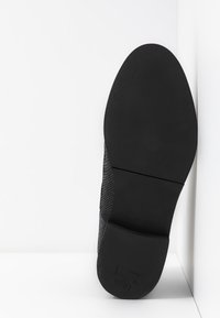 Czarne siatkowe buty o teksturowanej powierzchni i gładkiej, solidnej czarnej gumowej podeszwie, z okrągłym czubkiem i minimalistycznym designem.