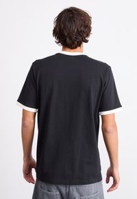 Camiseta de algodón negra con un escote redondo y puños blancos en contraste. Corte casual, textura suave y sin patrones o gráficos visibles.