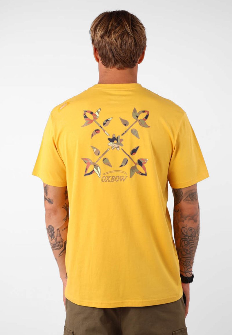 T-shirt en coton jaune avec un design graphique multicolore au dos, comportant des motifs floraux et la marque "Oxbow" au centre.