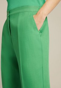 Pantaloni ampi in lino verde con tasche laterali, caratterizzati da una texture liscia e una vita rifinita con un bottone.