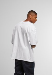 Volně střižené bílé bavlněné tričko s krátkými rukávy, kulatým výstřihem a rovnou spodní částí, nošené s modrými džínami z denimu.