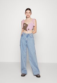 Top cropped de crochê em rosa e castanho com detalhes arredondados. Combinado com calças largas de ganga azul-claro e calçado escuro. Design simples e casual.