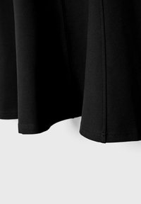 Panneaux de tissu noir avec des coutures et des ourlets visibles suspendus sur un fond clair, montrant la texture et les détails des points.