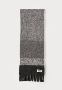 Grå uldscarf med et gradueret design, der har forskellige nuancer af grå. Afsluttet med frynser og et lille mærke nederst.