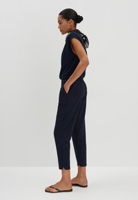 Ensemble de jogger bleu marine avec des manches courtes, un pantalon à taille élastique et des poches latérales. Le tissu semble doux, avec une texture lisse et un design minimal.