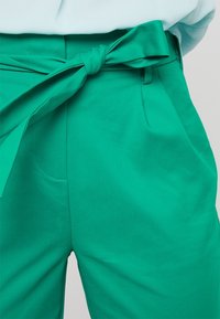 Pantalones verdes de cintura alta con un cinturón de tela. Cuenta con una textura suave, bolsillos laterales y un diseño entallado con una cintura ajustada.