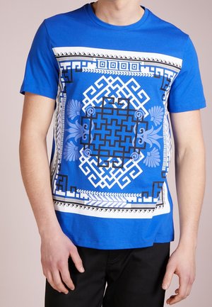 Niebieska bawełniana koszulka z geometrycznym i kwiatowym wzorem w czerni i bieli, z krótkimi rękawami i okrągłym dekoltem.