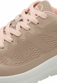 Sneaker mit beigem und hellrosa Farbschema. Verfügt über ein strukturiertes Mesh-Obermaterial, wellenförmige Designakzente und eine weiße Gummisohle.