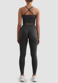 Komplet ciemnoszarej odzieży sportowej z prążkowanym crop topem z krzyżującymi się ramiączkami oraz legginsami z wysokim stanem, oba wykonane z gładkiego, elastycznego materiału.