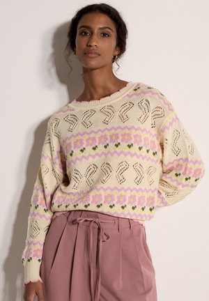 Pull en maille crème avec des motifs floraux en rose et vert, présentant une coupe ample, un col rond et des détails complexes rappelant de la dentelle.