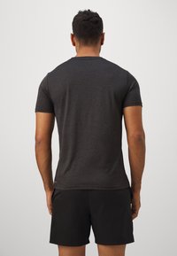 Tricou sportiv gri cu mânecă scurtă, cu o textură netedă, guler rotund și tiv rotunjit, asortat cu pantaloni scurți negri.