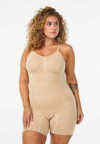 Bež bodysuit za oblikovanje tijela s podesivim naramenicama, koji ima rebrastu teksturu i bešavnu izradu, pružajući pokriće do sredine bedara.