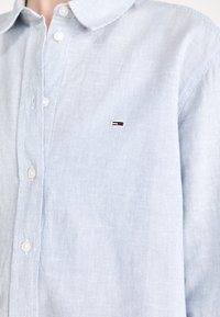 Camicia a strisce azzurre realizzata in tessuto intrecciato, con colletto button-down, bottoni bianchi e un piccolo logo ricamato sul petto.