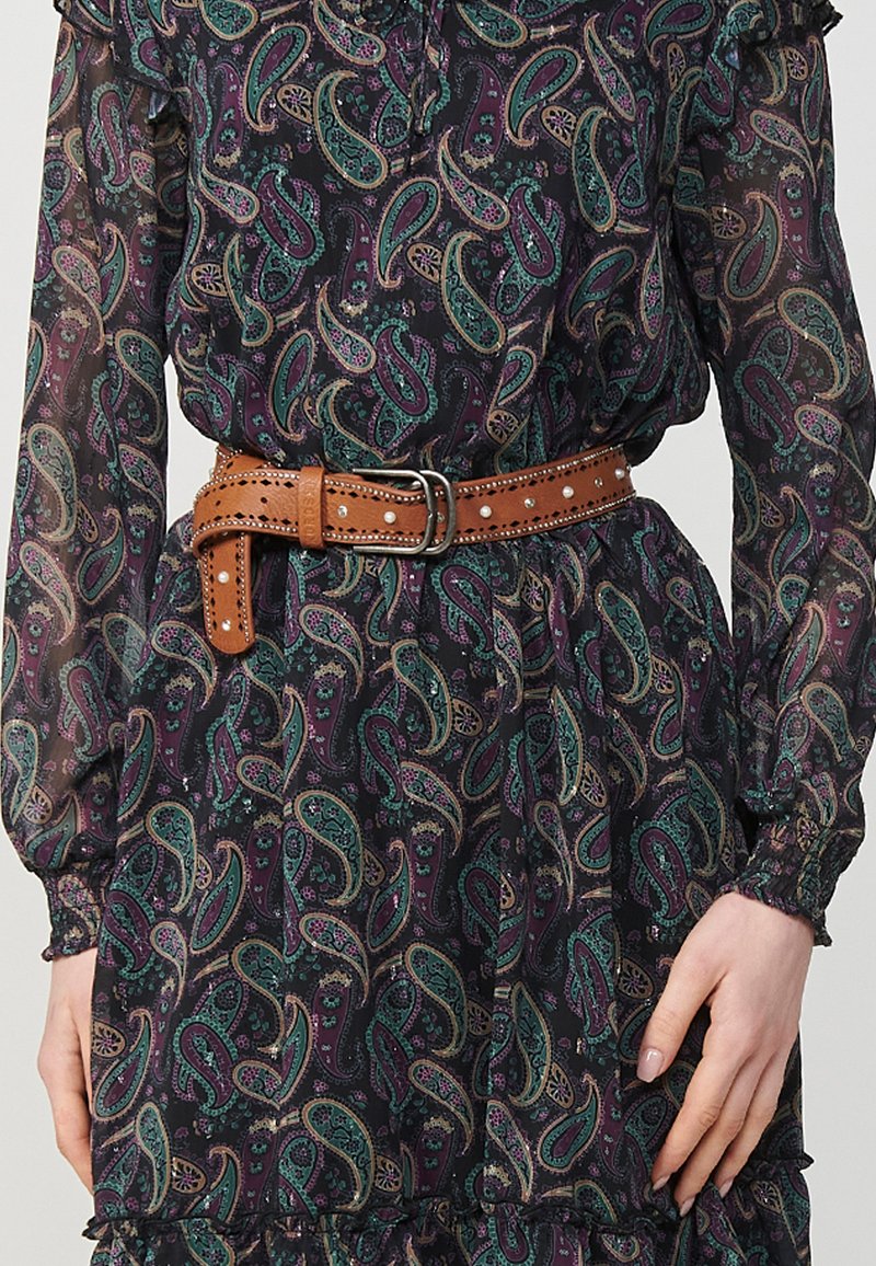 Vestido oscuro con un patrón de diseños paisley en tonos verde azulado, púrpura y dorado; ceñido con un cinturón de cuero beige adornado con tachuelas y una hebilla plateada.