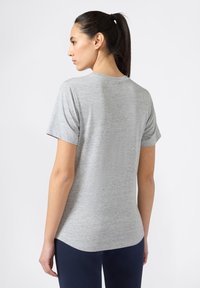 Szary t-shirt z krótkim rękawem o gładkiej fakturze, z okrągłym dekoltem i lekko zaokrąglonym dołem, zestawiony z ciemnymi spodniami.
