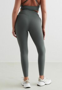 Hoge taille, figuur-volgende legging in olijfgroen, gemaakt van glad, rekbaar materiaal met een brede tailleband en gedetailleerde stiksels.