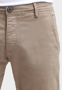 Beige bomullsbyxor med slät fram och standardmidjeband med knappstängning samt sidfickor med ren sömnadsdetalj.