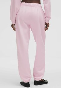 Rózsaszín, puha anyagból készült melegítőnadrág, rugalmas derekú és szűkülő szárú, sima tapintású és kényelmes kialakítással.