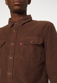 Braunes Cordhemd mit durchgehendem Knopfverschluss, Kragen und zwei Brusttaschen mit einem kleinen roten Levi's-Logo-Tag. Strukturiertes, geripptes Gewebe.