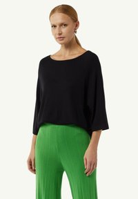 Schwarzes, lockeres Oberteil mit weitem Ausschnitt und drei Viertelärmeln, kombiniert mit hellgrünen, gerippten, hoch taillierten Hosen.