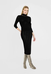 Mustast mosaiikidest kleit, millel on keha järgiv siluett, vertikaalne soonik ja kõrge kaelus. Kandke koos põlveni ulatuvate mustriliste maduprintsaabastega.