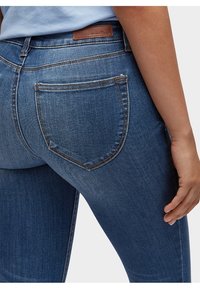 Jeans i denim i mörkblått med en åtsittande design. Har en bakficka och en läderlapp på midjan. Slät textur, klassisk stil.