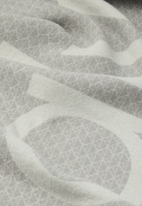 Material moale cu modele geometrice subtile în nuanțe de gri deschis și alb, prezentând pliuri ușoare și detalii de textură.