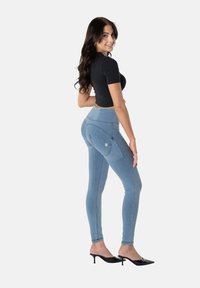 Vaqueros ajustados azul claro con cintura alta, costuras decorativas, bolsillos traseros y un logo sutil. Combinados con un top corto negro.