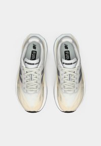 Une paire de chaussures de course New Balance FuelCell Rebel blanches et beiges avec des accents gris, vues du dessus sur un fond blanc.