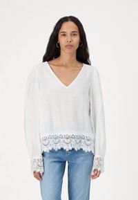 Witte blouse met lange mouwen en V-hals, voorzien van kantafwerking bij de manchetten en onderkant. Zachte stof met een losse pasvorm en een gestructureerd detail.