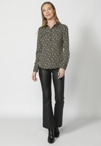 Camicia a maniche lunghe con stampa floreale nera, colletto e design aderente, abbinata a pantaloni neri a campana e stivaletti.