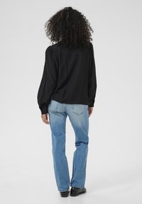 Black long-sleeve blouse with a relaxed fit and puffed shoulders, paired with blue straight-leg jeans and black shoes.