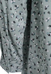 Floral-patterned blouse in light green fabric. Features small black, white, and blue flowers with a buttoned cuff detail on the sleeve.