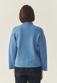 Pull bleu clair avec un col montant, des manches larges et un ourlet côtelé ; fabriqué dans un tissu doux ; design simple et épuré.