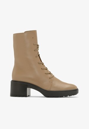 Valkoinen nahkainen nilkkuri, jossa on pyöreä kärki, nauhoitus etupuolella ja paksu musta korko. Ominaisuuksiin kuuluu sileä pinta ja minimaalinen yksityiskohtaisuus.