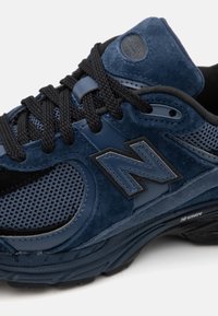 Zapatillas de ante azul y malla con acentos negros, cordones texturizados y una suela acolchada. Presenta el logo de "N" en el lateral.