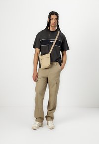 Black short-sleeve t-shirt with white horizontal stripes, beige cargo pants, and a small beige shoulder bag. Worn with beige sneakers.