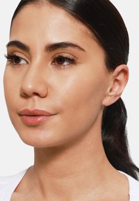 Goldene Sternohrringe an einem Modell. Die Ohrringe haben ein minimalistisches Design. Das Modell hat einen natürlichen Teint und trägt ein weißes Oberteil.