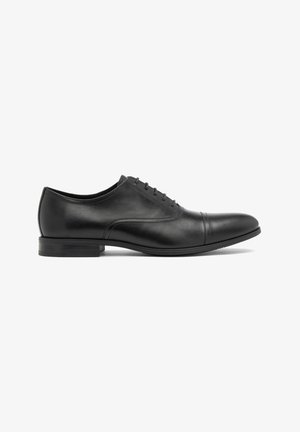 Zwarte leren dress shoe met een gladde afwerking, afgeronde neus, vijf vetersleuven en een subtiele naad aan de zijkant; platte rubberen zool.