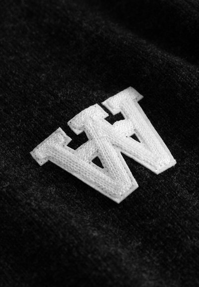 Fond en tissu noir avec un logo "W" blanc brodé en évidence, présentant une finition texturée et des angles prononcés.
