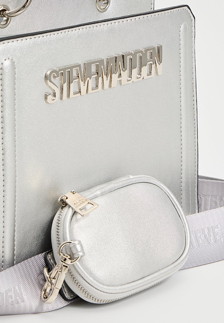 Sac à main argenté avec une finition brillante, mettant en valeur le logo en relief "STEVE MADDEN", accompagné d'une petite pochette à pièces détachable.