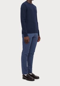 Marinblå tröja med rund hals, texturerad tyg. Matchad med ljusblå chinos och mörka loafers, som visar en polerad, skräddarsydd look.